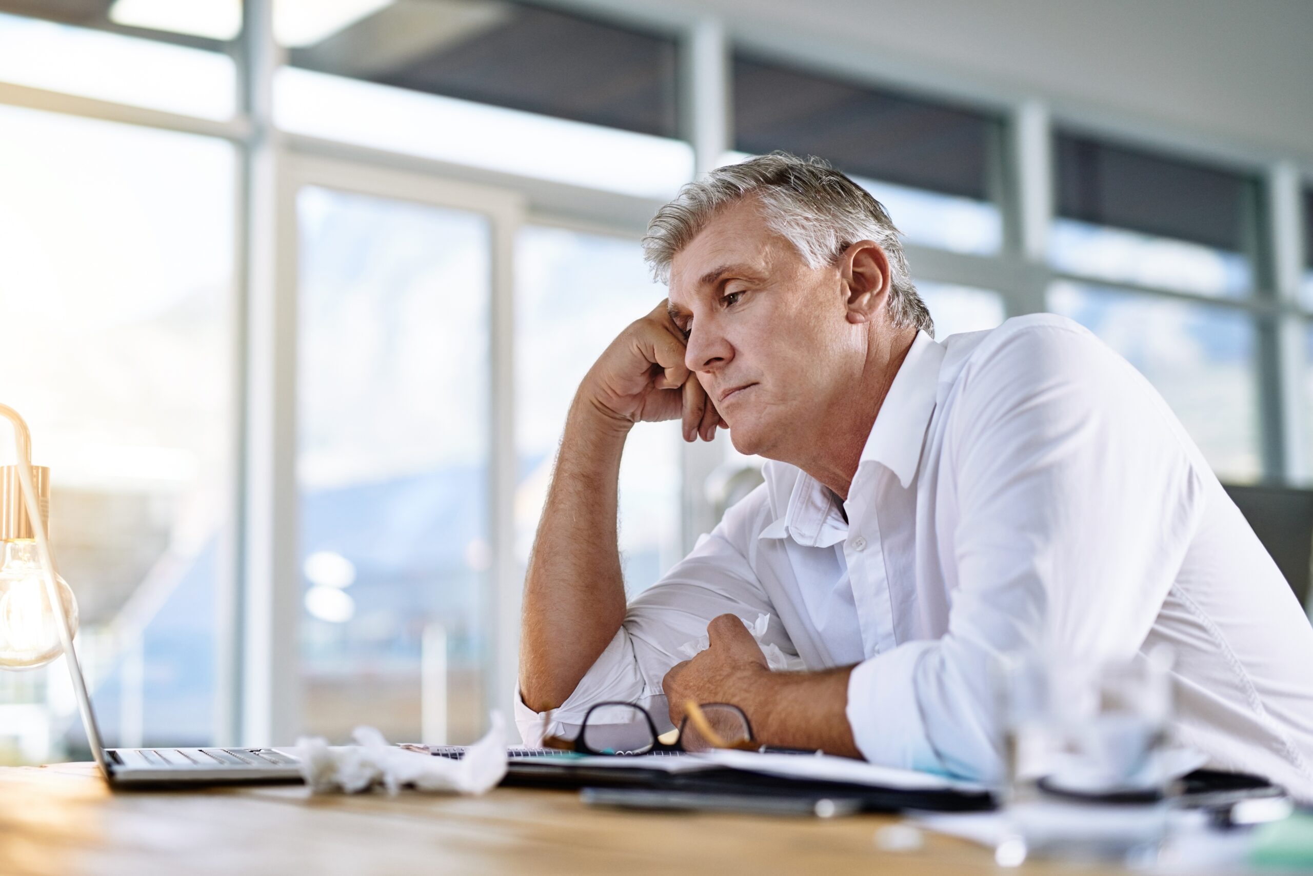 Mature businessman looking tired while working on a laptop, showing fatigue and poor sleep quality.