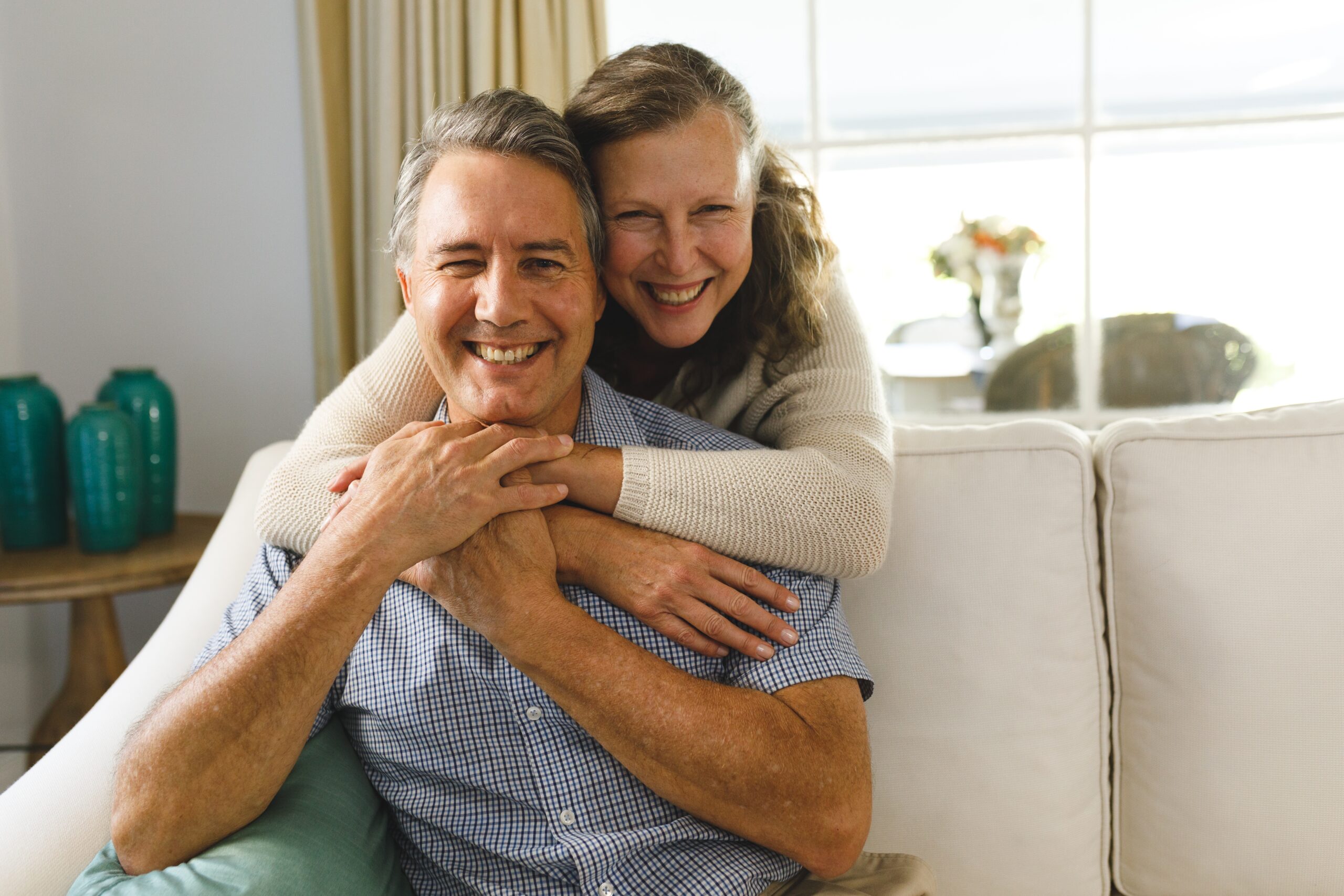 Happy senior Caucasian couple sitting together on a sofa in a bright living room, smiling and relaxed in their home.